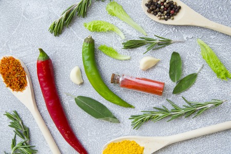 Dry spices and herbs in wooden spoons and glass jar, fresh herb springs, chili pepper and garlic on a light stone background with copy space, top view, flat layの写真素材