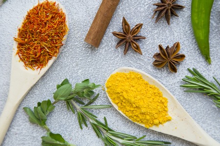Dry spices and herbs in wooden spoons with fresh herb springs, cloves and cinnamon on a light stone background with copy space, top view, flat layの写真素材