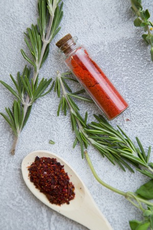 Dry spices and herbs in wooden spoons and glass jars with fresh herb springs on a light stone background with copy space, top view, flat layの写真素材