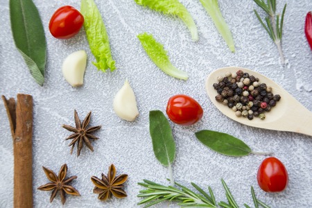 Dry pepper corns in a wooden spoon, fresh herbs springs, cherry tomatoes, cinnamon and garlic on a...