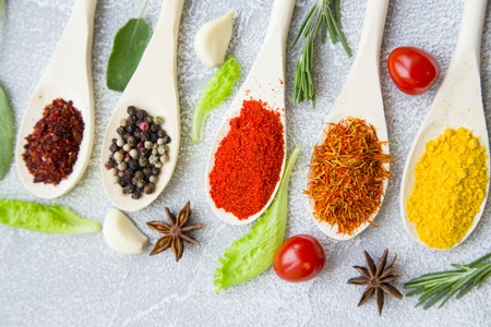 Dry spices and herbs in wooden spoons with fresh herb springs, cherry tomatoes, cinnamon and garlic...