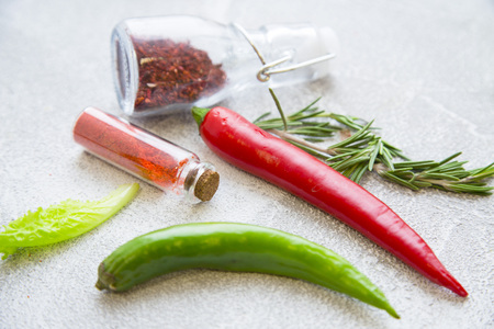 Dry spices and herbs in glass jars with fresh herb springs and chili peppers on a light stone background with copy space, close upの写真素材