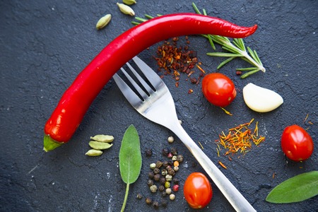 Pinches of dry spices, cherry tomatoes, beans, red chilli pepper and a fork on a black stone background with copy space, top view, flat layの写真素材