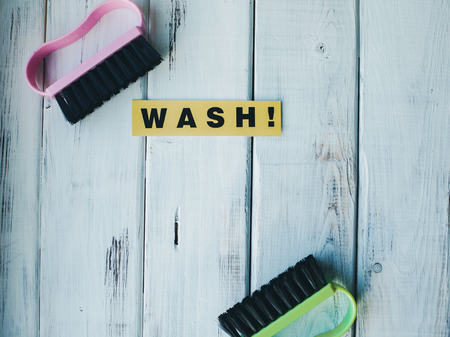 Cleaning house or office concept. Pink and green cleaning brushes and WASH inscription on a white wooden background. Top view, closeupの写真素材