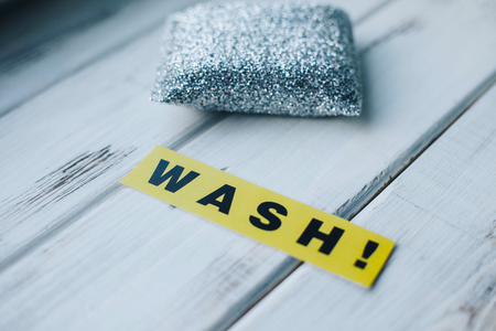 Cleaning house or office concept. Steel scrub sponge and WASH inscription on a white wooden background. Top view, closeupの写真素材