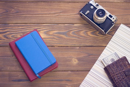 Get ready for vacation. Red and blue notepads, a vintage photo camera and a leather wallet with money on a wooden table, top viewの写真素材