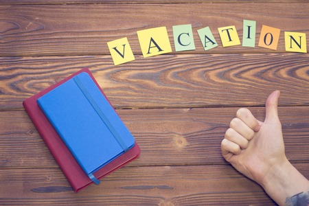Get ready for vacation. Red and blue notepads, Vacation inscription and a woman's hand showing a thumb up on a wooden table, top viewの写真素材