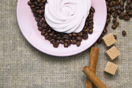 Love Coffee Concept. A pink saucer with coffee beans and a murshmellow, sugar cubes and cinnamon on burlap fabric background, close up, top viewの写真素材