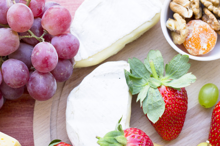 Snacks with wine - Strawberry, various types of cheeses, figs, nuts, honey, grapes on a red wooden backgroundの写真素材