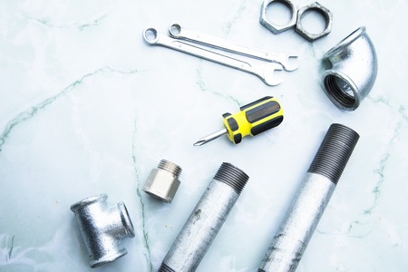 Various plumbers tools and plumbing materials including stainless steel pipe, elbow joint, wrench and spanner. Bright white marble background. Top view, copyspaceの写真素材
