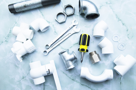 Various plumbers tools and plumbing materials including stainless steel and plastic PVC pipe, elbow joint, wrench and spanner. Bright white background. Top view, copyspaceの写真素材