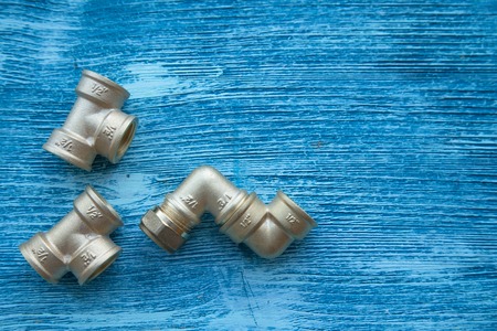 Various plumbers tools and plumbing materials including stainless steel pipe, elbow joint, wrench and spanner. Blue wooden background. Top view, copyspaceの写真素材