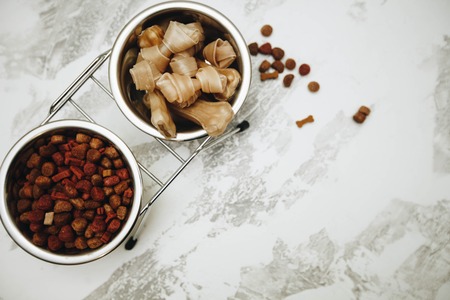 Dry pet food and chewing bones in bowl on white wooden background top view copyspaceの写真素材