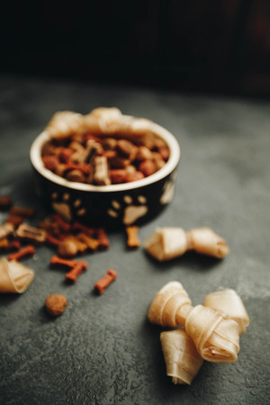 Dry pet food in bowl and chewing bones on dark stone background top view copyspaceの写真素材