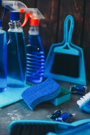 Cleaning house or office concept. A set of blue cleaning supplies against a dark wooden wall, close...