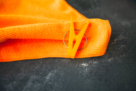 Cleaning house or office concept. An orange cleaning rag and a clothes peg on a dark concrete background, top view, close upの写真素材