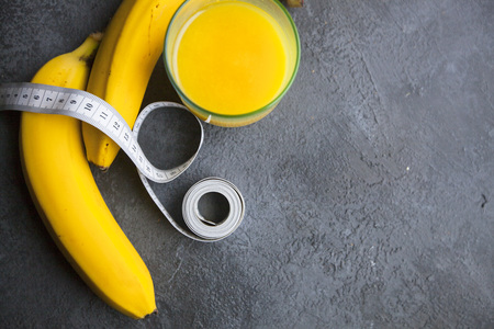 Healthy Breakfast, Sport, Fitness, Weight Loss, Diet Concept. Keeping fit with bananas, a glass of orange juice and tape-measure, dark stone backgroundの写真素材