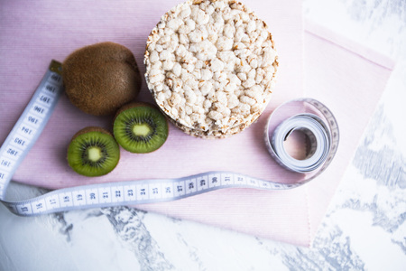 Healthy Breakfast, Sport, Fitness, Weight Loss, Diet Concept. Fresh kiwi, bread crisps and tape-measure ,white stone background, top viewの写真素材