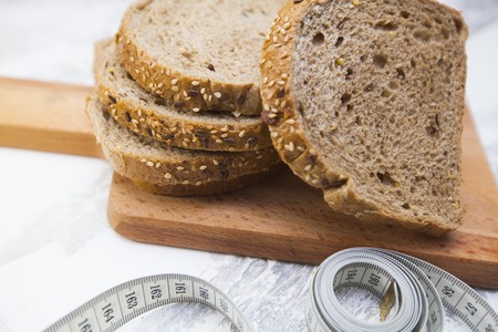Healthy Breakfast, Sport, Fitness, Weight Loss, Diet Concept. Sliced wholegrain bread on a cutting board and tape-measure ,white stone background, top viewの写真素材