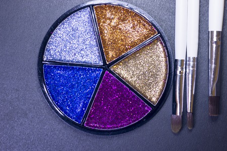 A palette of colorful glitter eyeshadow and profeccional make up brushes on a black background, close up, top viewの写真素材