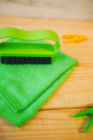 Cleaning house or office concept. A green plastic brush,a rag and clothes pegs on a natural wooden...