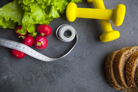 Healthy Breakfast, Sport, Fitness, Diet Concept. Fresh lettuce, sliced rye bread, radish, tape measure and yellow dumbbells , dark stone background, close up, top viewの写真素材
