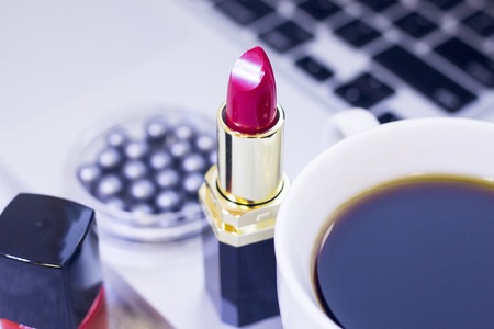 Make Up Beauty Fashion Business Concept. Matte lipstic, nail polish and pearl grey eyeshadow on a white table with laptop and coffee cup, close upの写真素材