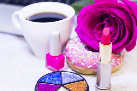 Make Up Beauty Fashion Business Concept. Pink nail polish, lipstick and a glitter box on a white table with laptop, coffee cup, donut and a pink rose, close upの写真素材