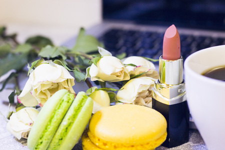 Make Up Beauty Fashion Business Concept. Nude lipstick, macaroons, coffee cup and white roses, close up, laptop in the backgroundの写真素材