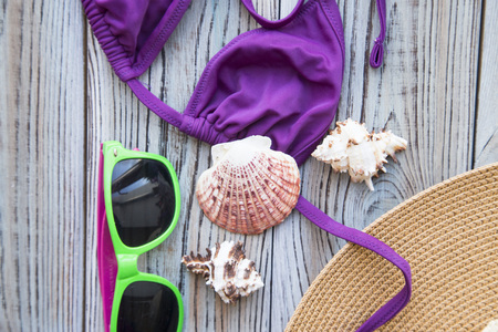 Vacation concept. Green sunglasses, purple swim suit and sea shells on a grey wooden background, copy spaceの写真素材