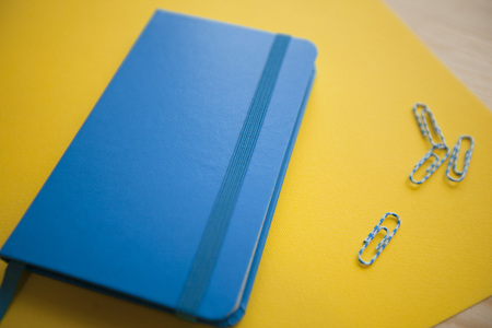 Education Creativity concept. Blue notepad and paper clips on a yellow paper, light wooden...