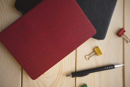Education Creativity concept. Red and black notepads, pen and colorful paper clips on a light wooden background, close up, top viewの写真素材