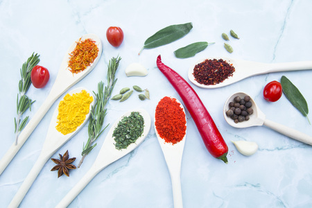 Cooking Hot Spicy Food Concept. Dry spices and herbs in wooden spoons, fresh herbs, chili peppers and beans, white marble background, top view, mock upの写真素材