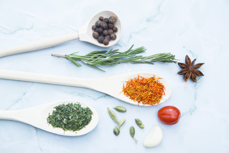 Cooking Hot Spicy Food Concept. Dry spices and herbs in wooden spoons, fresh herbs and beans, white marble background, top view, mock upの写真素材
