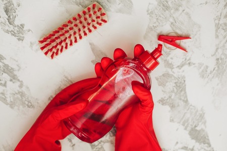 Cleaning house or office concept. Hands in red rubber gloves holding a red bottle of dishwashing liquid, white stone background, top viewの写真素材