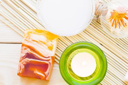 Spa and wellness setting with yellow flower, green candle, oil and soap on wooden white background...