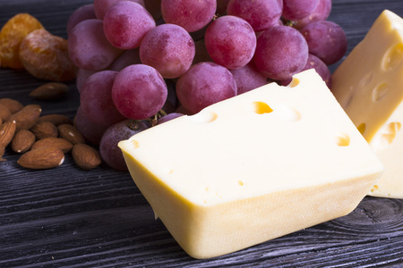 Cheese cuts with figs, nuts, honey, grapes on a dark rustic wooden boards background. Top view