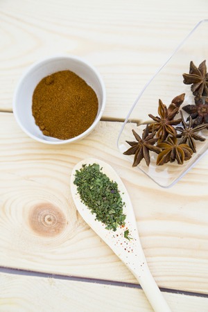 Cooking Hot Spicy Food Concept. Dry spices, beans and herbs in wooden and glass spoons and palstic cup on light wooden table, top viewの写真素材