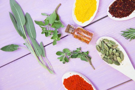 Cooking Hot Spicy Food Concept. Dry spices,beans and herbs in glass jar with cork,plastic cup and wooden spoons, purple wooden background, top viewの写真素材