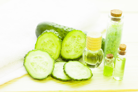 Cucumber home spa and hair care concept. Sliced cucumber, bottles of oil, jar of mask, bathroom towel. White board background. Closeupの写真素材