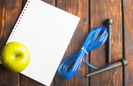 Time for diet slimming weight loss concept. Sport fitness, apple, sneakers, bottle of water and yellow weights on dark wooden backgroundの写真素材