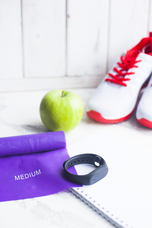 Time for diet slimming weight loss concept. Sport fitness, apple, sneakers, bottle of water and yellow weights on white wooden backgroundの写真素材