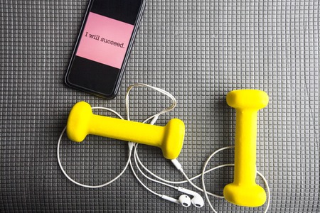 Time for diet slimming weight loss concept. Sport fitness, apple, sneakers, bottle of water and yellow weights on grey rubber background.の写真素材
