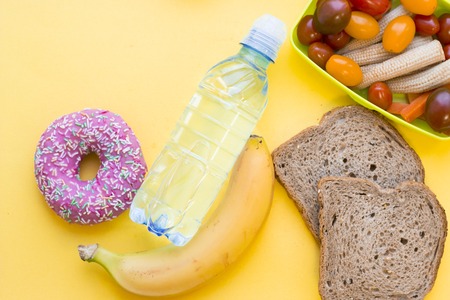 School lunch box. Bread, a bottle of water, candies, baby corns, carrot and tomatoes in green...