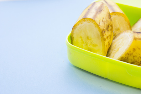 School lunch box. Bread, orange, candies, baby corns, carrot and tomatoes in green plastic container. Top view, blue backgroundの写真素材