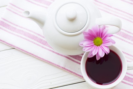 Black tea ceremony - a cup of tea, teapot, sugar, cakes, flowers on white wooden rustic background, top view, closeupの写真素材