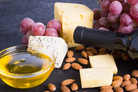 Snacks with wine - bottle, various types of cheeses, figs, nuts, honey, grapes on a black stone backgroundの写真素材