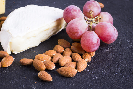 Snacks with wine - various types of cheeses, figs, nuts, honey, grapes on a black stone backgroundの写真素材