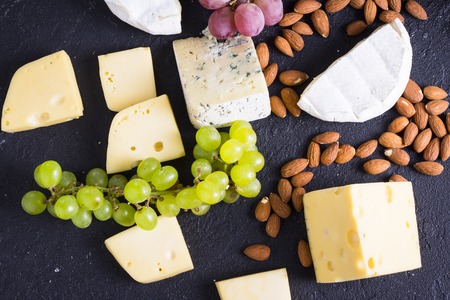 Snacks with wine - various types of cheeses, figs, nuts, honey, grapes on a black stone backgroundの写真素材