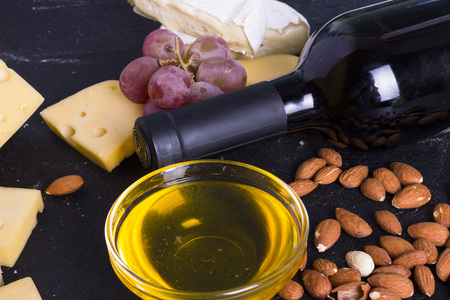 Snacks with wine - bottle, various types of cheeses, figs, nuts, honey, grapes on a black stone backgroundの写真素材